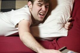 man hitting snooze on his alarm