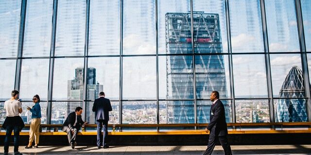 man walking down the hall of an office building with huge glass windows behind him