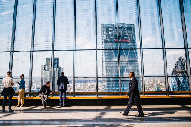 man walking down the hall of an office building with huge glass windows behind him