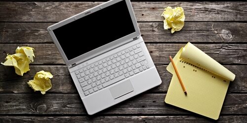 Overhead view of a laptop and a notebook sitting on a wooden table