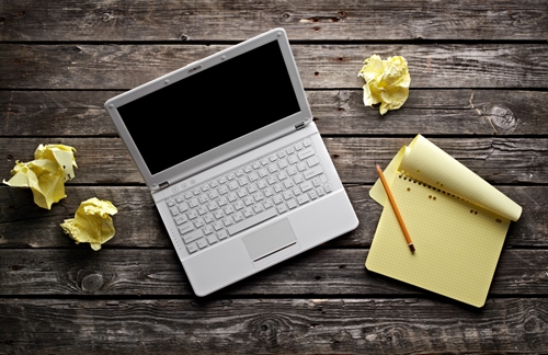 Overhead view of a laptop and a notebook sitting on a wooden table