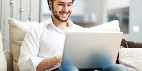 man smiling as he works at his laptop on his couch
