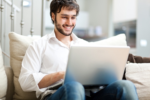 man smiling as he works at his laptop on his couch