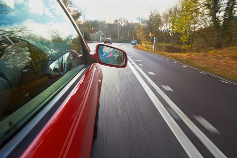 side of a red car driving down a road in the fall