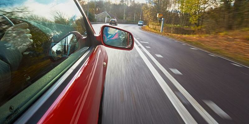 side of a red car driving down a road in the fall