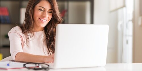 woman smiling at her laptop as she works in a bright office