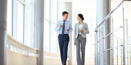 man and woman walking down a bright hallway talking