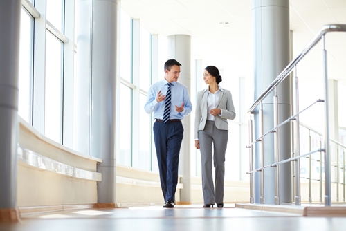 man and woman walking down a bright hallway talking