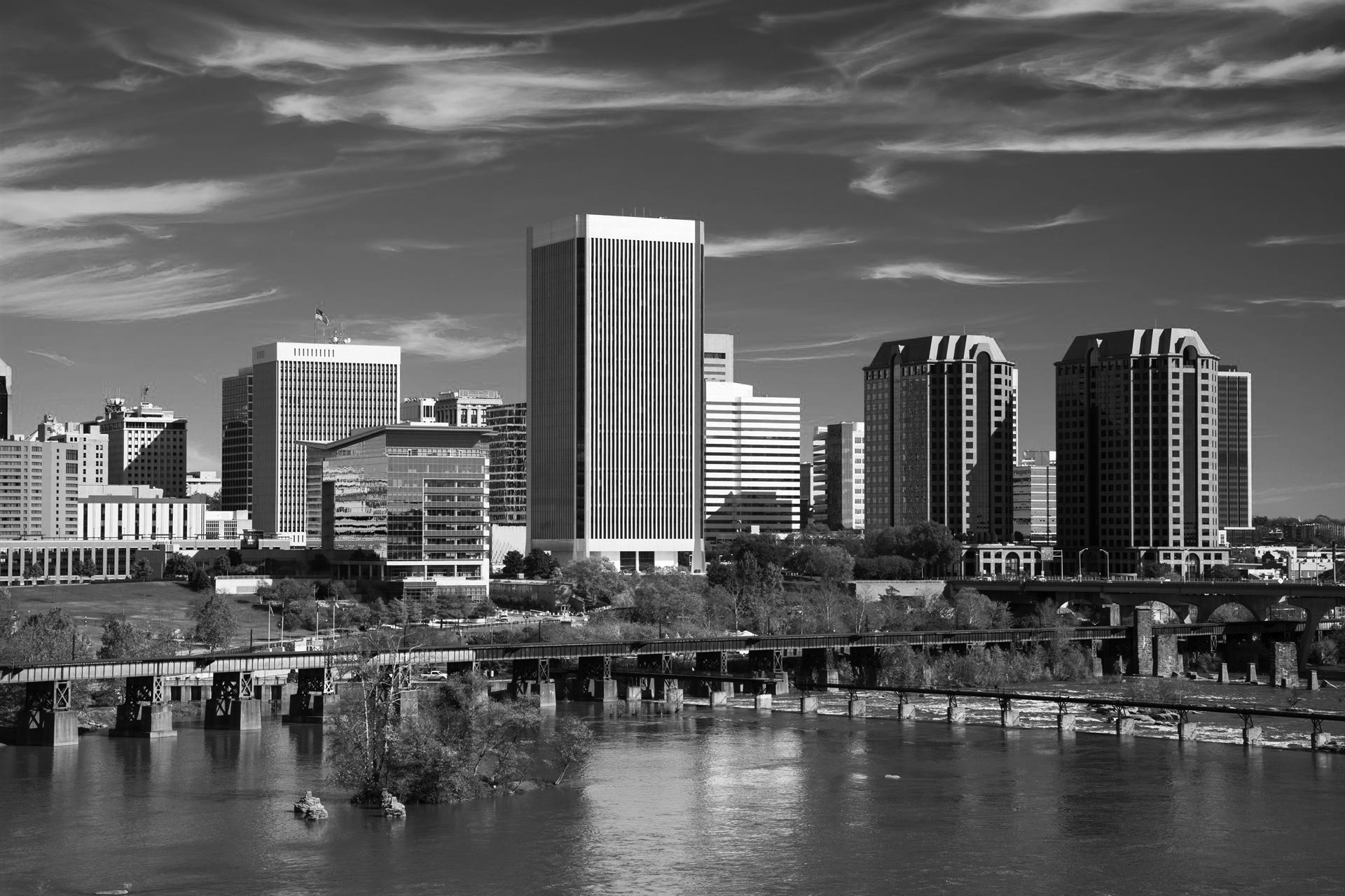 Downtown Richmond skyline closeup view with the James River in the foreground and a blue sky with wispy clouds in the background. Picture taken in Autumn.