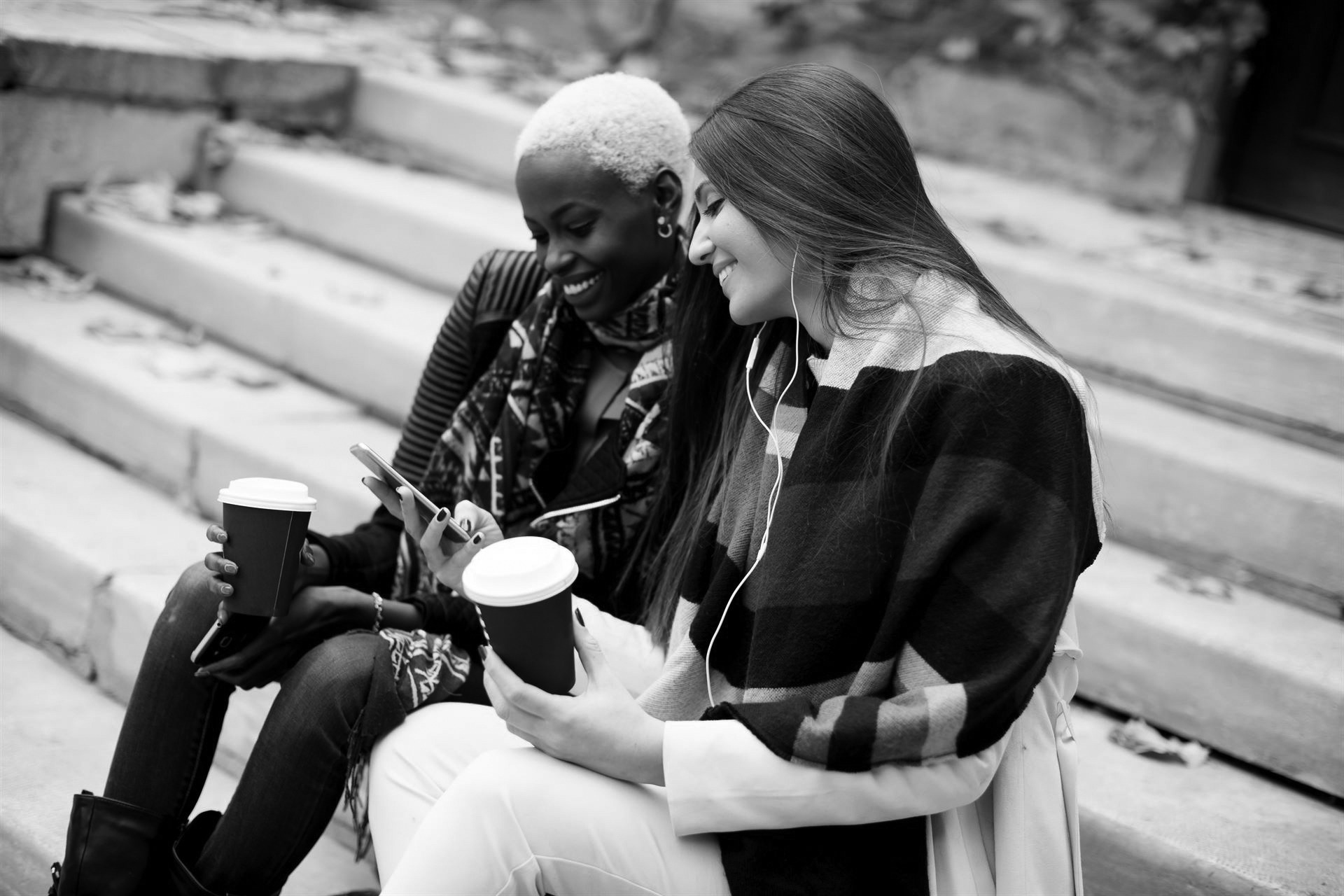 Young friends sitting in autumn park, talking and carry coffee to go in the hands