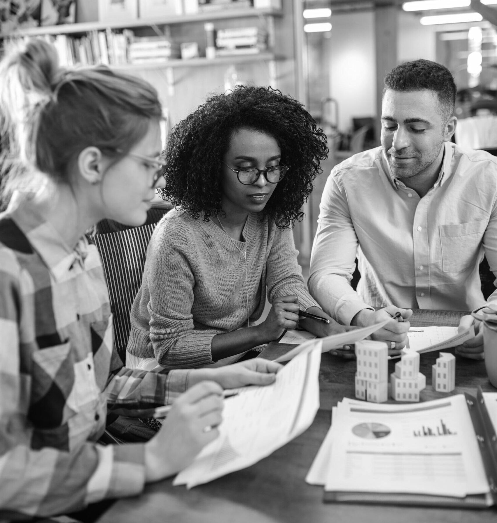 3 young business professionals crowded around the table going over data paperwork in a library.