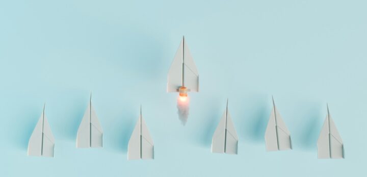 paper airplanes in a line with one taking off to symbolize leadership